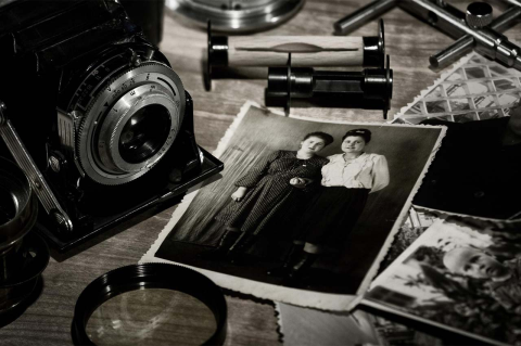 A black and white image of a vintage camera and snapshots of people from early in the 20th century. 