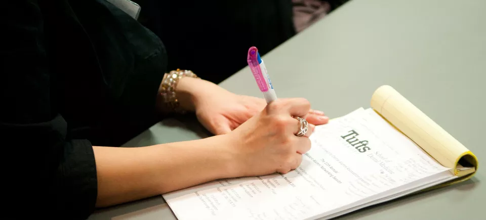 A person writing in a Tufts University notepad