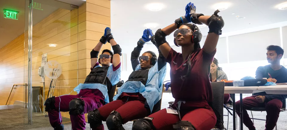 Three students perform tasks while wearing suits designed to simulate challenges associated with aging