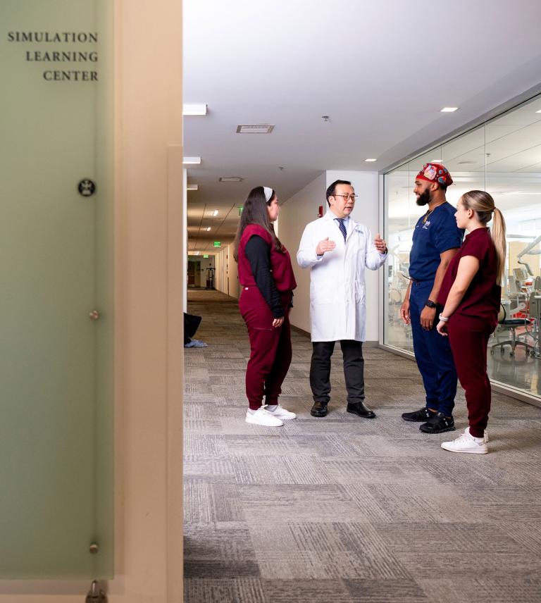 A professor speaking to three students in the Simulation Learning Center