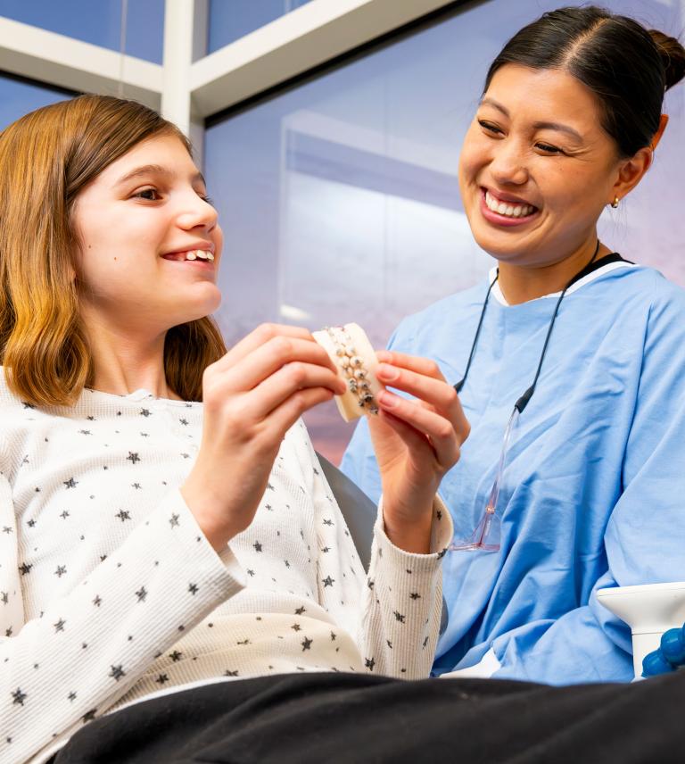 A dentist smiling and a child holding model teeth with braces