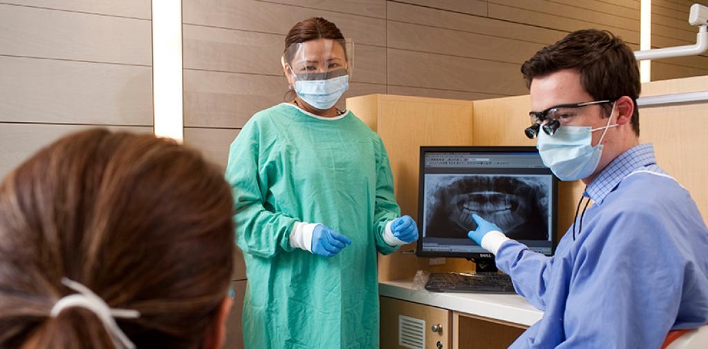 Dentist explaining his work to his patient while assistant stands by