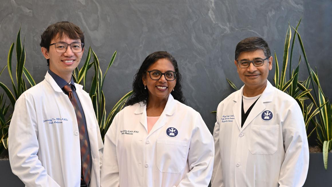 Three dentists wearing white coats smiling in front of greenery