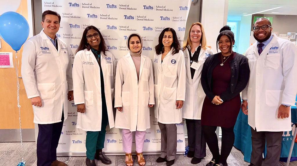 Seven people posing for a photo in front of a Tufts School of Dental Medicine backdrop