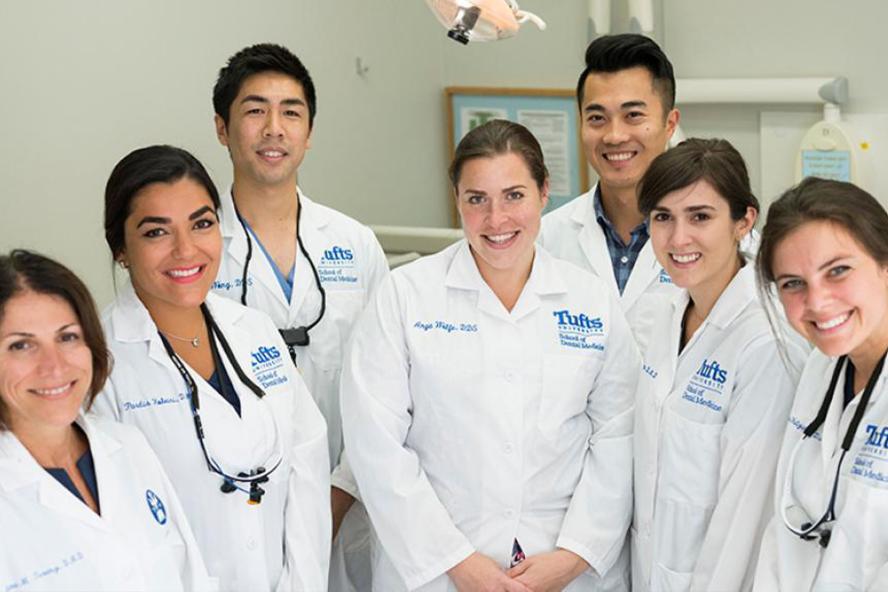 A group of dentists wearing white coats smiling and posing for the photo