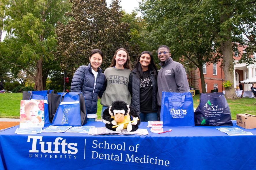 Dental students smiling while standing next to a table with bags and stuffed animals