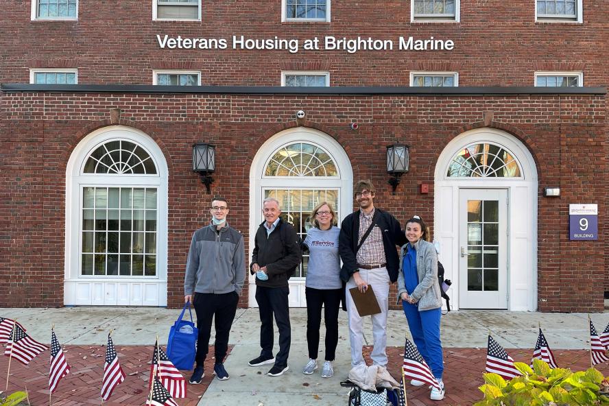 A group of people, smiling, standing in front of a building that reads Veterans Housing of Brighton Marine