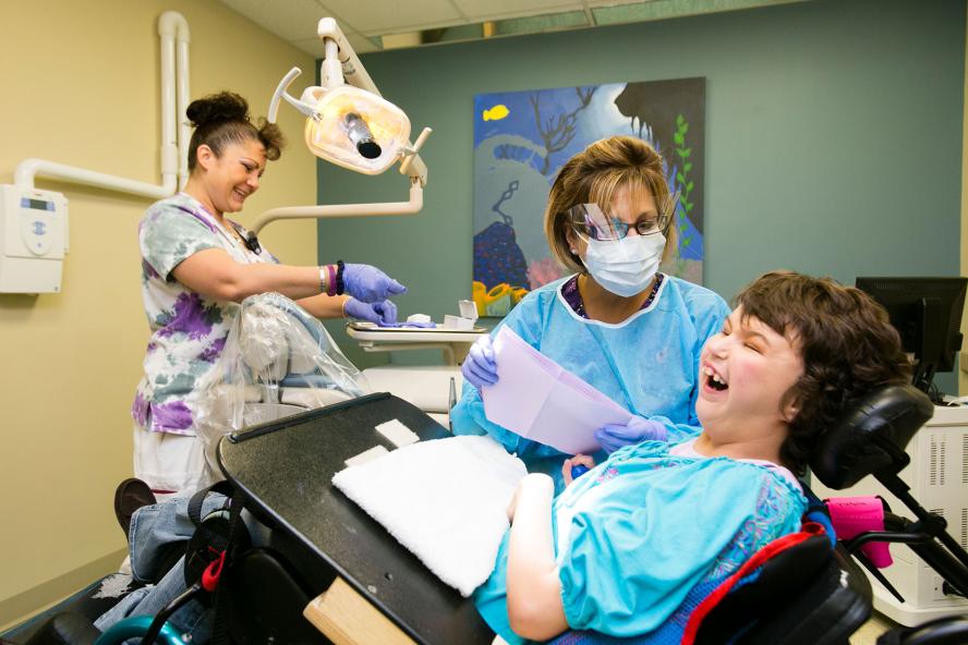 A dentist and an asisstant are treating a special needs patient, the assistant and patient are laughing