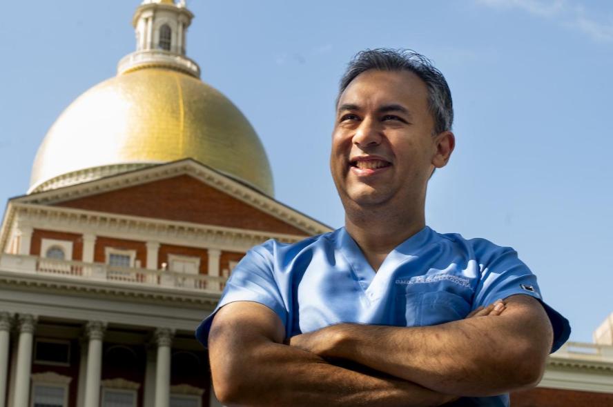 Abe Abdulwaheed in blue scrubs standing in front of the Massachusetts State House,