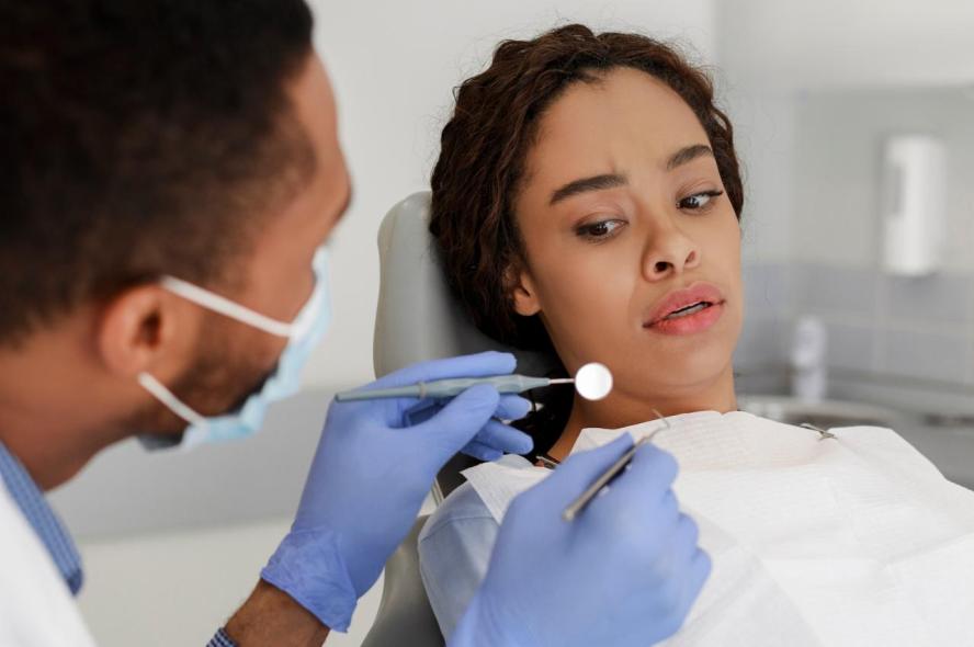 Woman looks warily as dentist holds out mirror.
