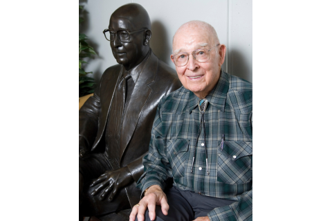 Dr. Robert D. Buchanan sitting next to statue of himself 
