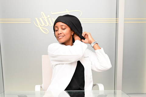 A woman in a dentist's white coat tucks her hair into a head covering.