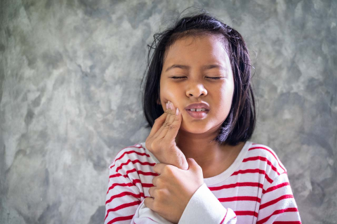 A young girl with a toothache rubs her face.