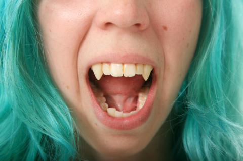 A woman with green hair and very long canine teeth