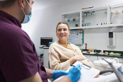 A pregnant woman sitting in a dental chair with a dentist holding a clipboard by her side.