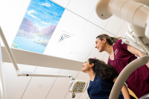 Two dental students gaze at a painting on the ceiling above a dental chair.