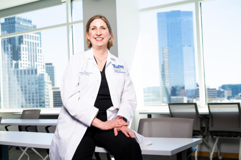 Melissa Newman in a white medical coat in front of a wall of windows