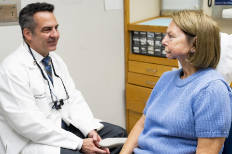 Daniel Oreadi, in a white coat, talking to Cathy Hapenney, sitting  in a dental chair